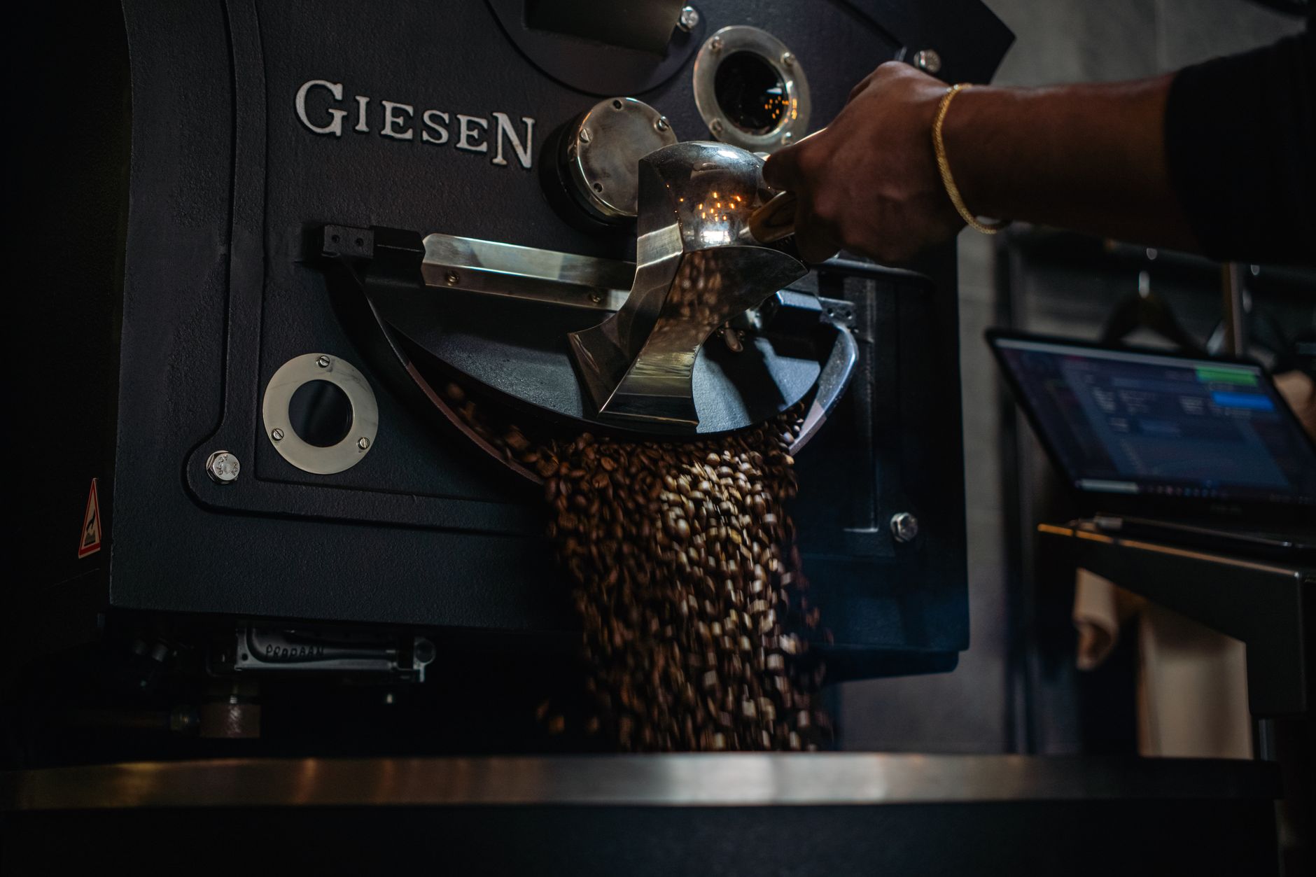 Close-up of coffee beans being roasted, a hand scooping them from the drum
